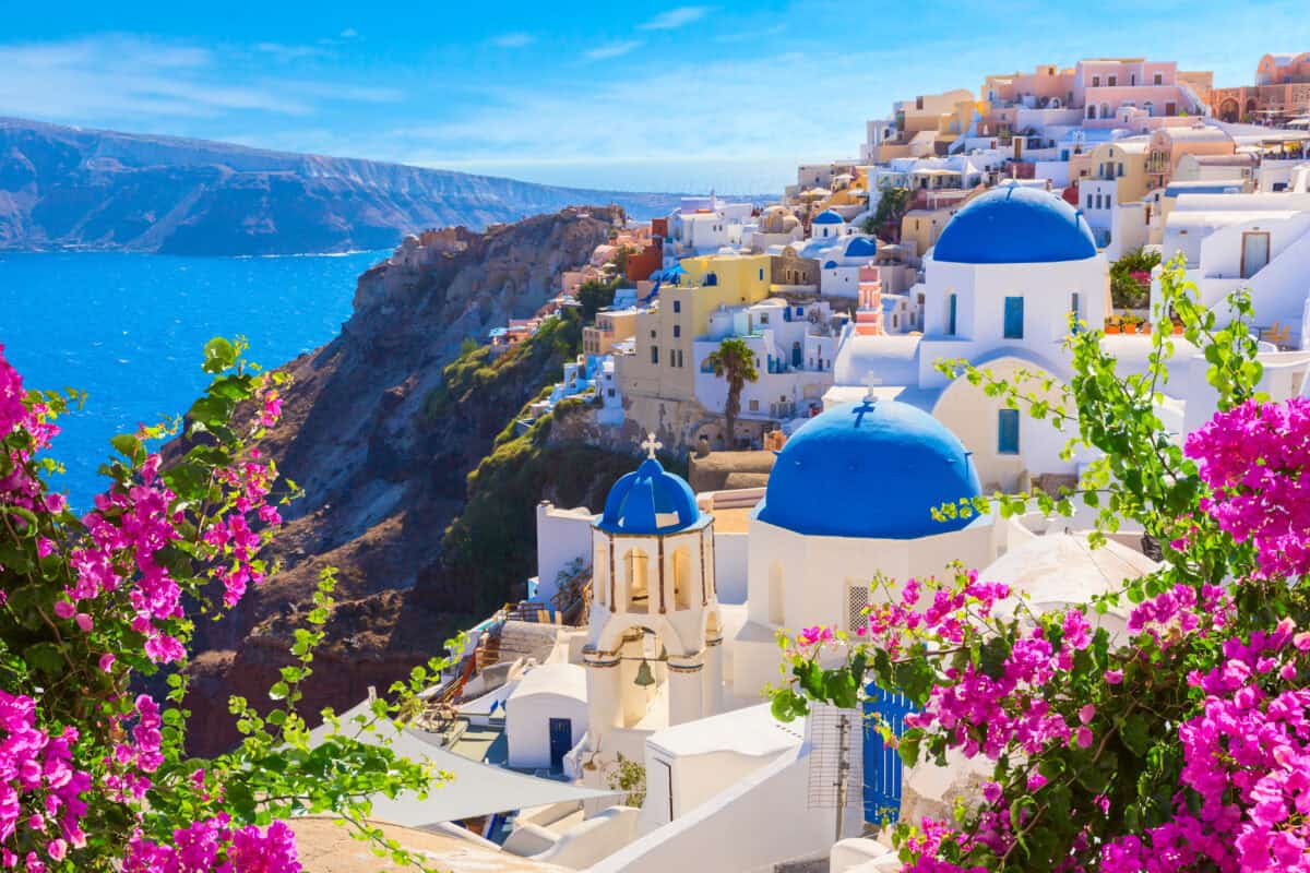 Santorini Oia with white houses, blue domes, caldera views, and vibrant Mediterranean flowers.