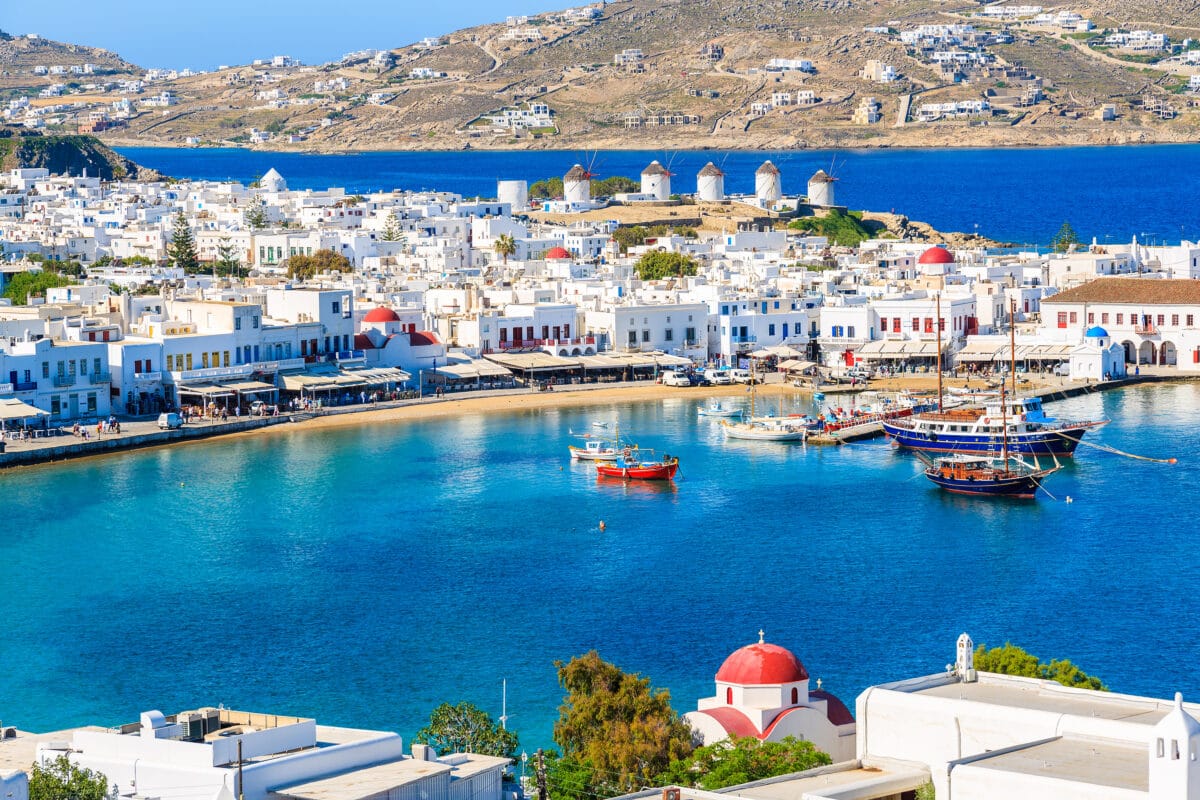 Mykonos port with boats, windmills, whitewashed buildings, and Greek island scenery.